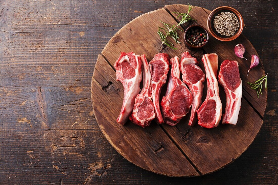 Raw fresh lamb ribs with pepper and cumin on wooden cutting board on dark background