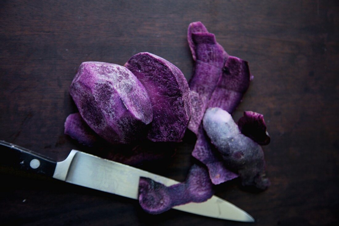 Lila Kartoffeln mit Messer auf dunklem Hintergrund