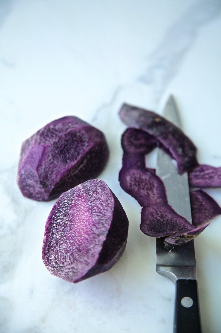 Purple potatoes, cut and peeled with knife on a white marble background