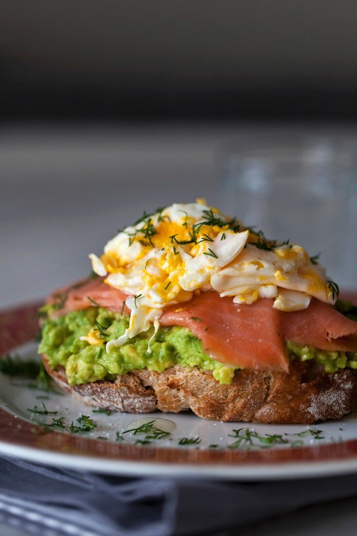 Sandwich of mashed avocado, smoked salmon and fried egg on a plate