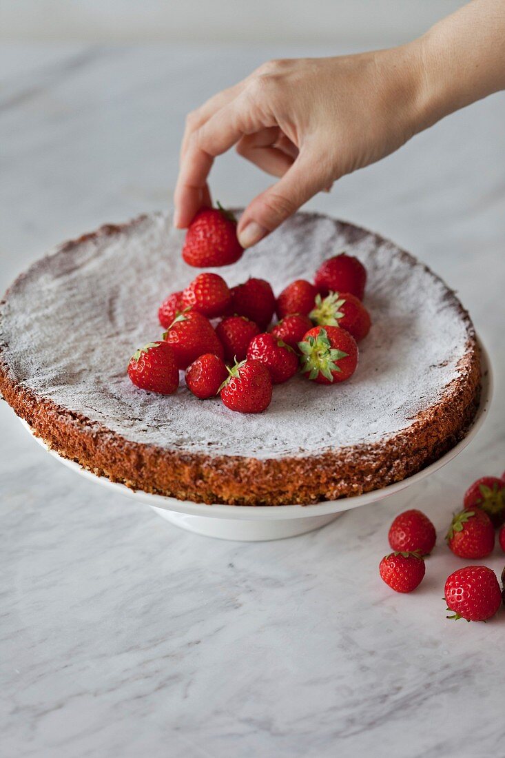 Almond cake topped with fresh strawberries on white stand, gluten-free