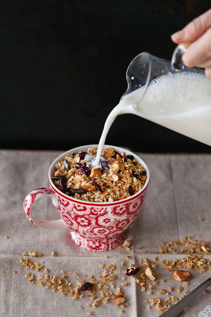 Almonds and cranberries homemade granola in a cup with milk pouring from a jar