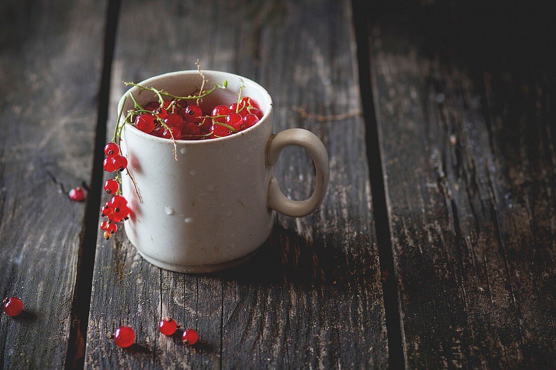 Old white cup full of fresh ripe red currant over old wooden table
