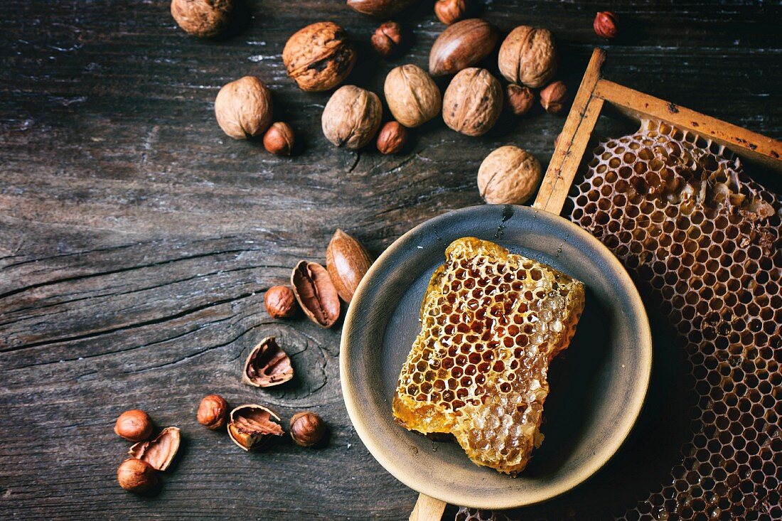 Honigwabe auf Keramikteller und verschiedene Nüssen auf altem Holztisch