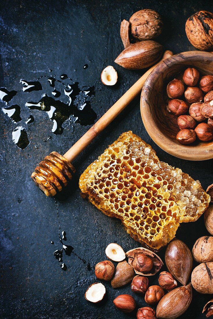 Honeycomb with honey dipper and mix of nuts over black surface