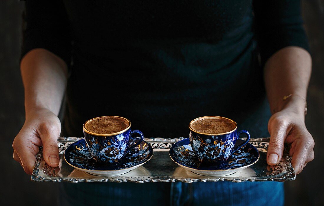 A woman serving two cups of Turkish coffee on a silver tray