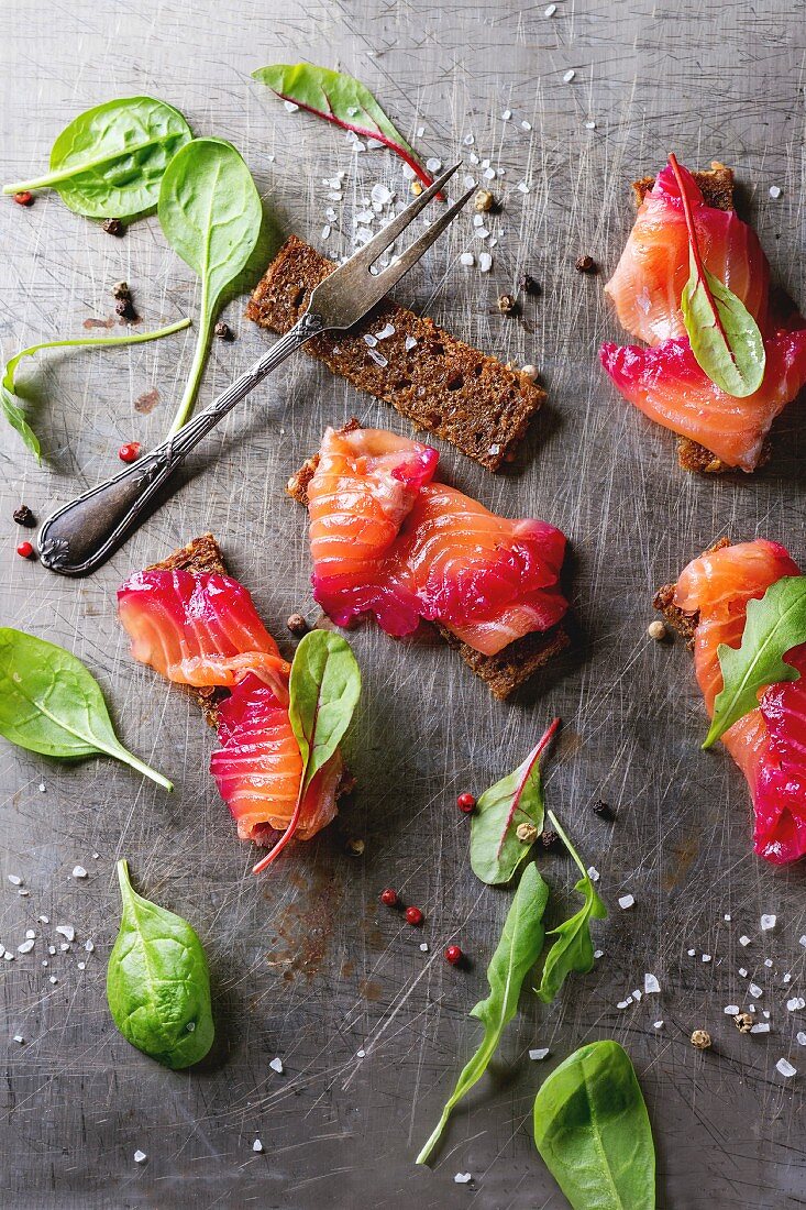 Sliced salmon filet, salted with beetroot juice, served on whole wheat toasts with salad leaves