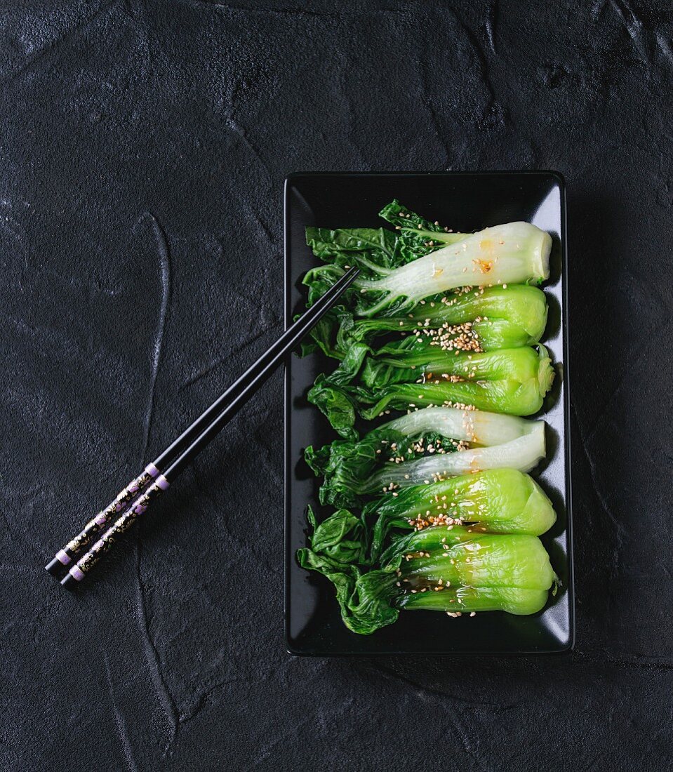 Pak Choi mit Sesam und Chiliöl auf schwarzer Platte mit schwarzen Stäbchen