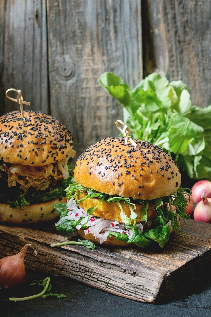 Two Homemade veggie burgers with sweet potato, fresh radish and pea sprouts, served on wooden chopping board