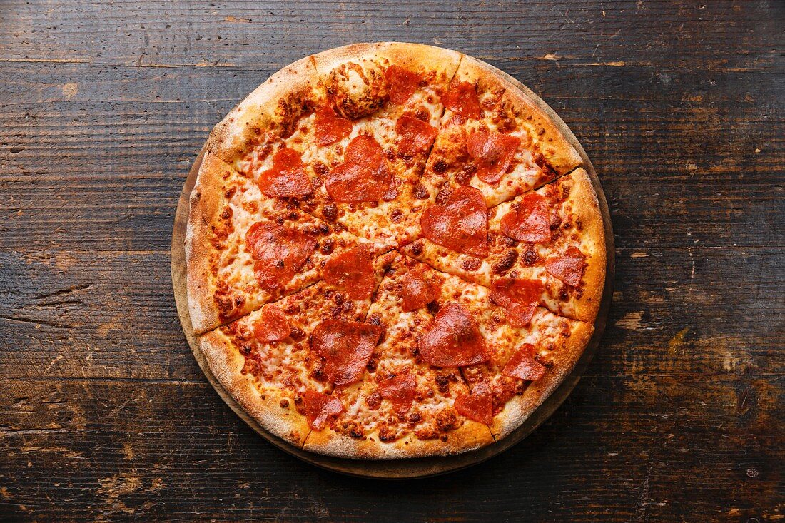 Pizza mit herzförmiger Peperoni-Salami auf Holzuntergrund
