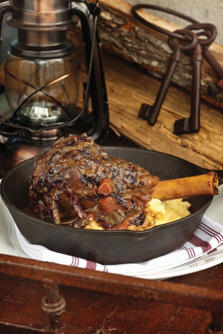 Radicchio braised lamb shank on black cast iron skillet with oil lamp in background
