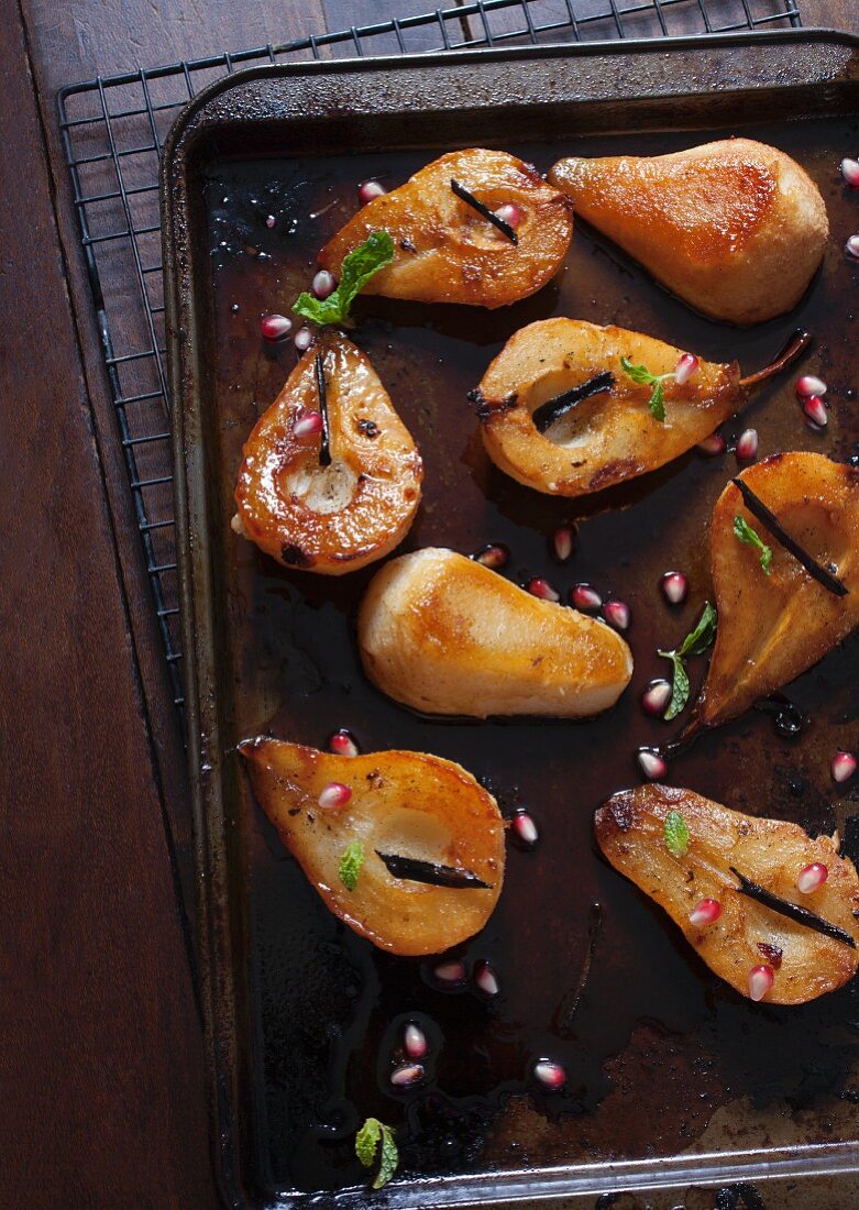 Halved roasted pears with pomegranate seeds and vanilla on a baking tray