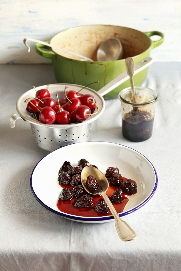 Cherry jam on a plate, fresh cherry in aluminum colander and dutch pot with cherry jam on background