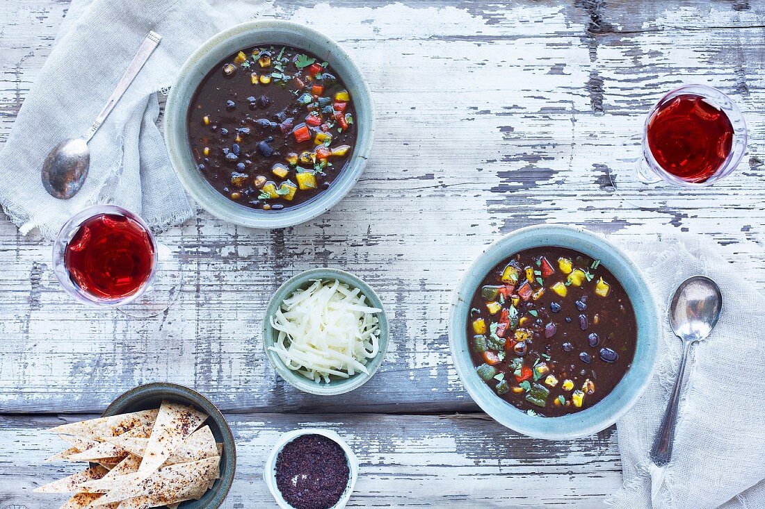 Black bean soup topped with roasted peppers, cilanrto and cheese in ceramic bowls