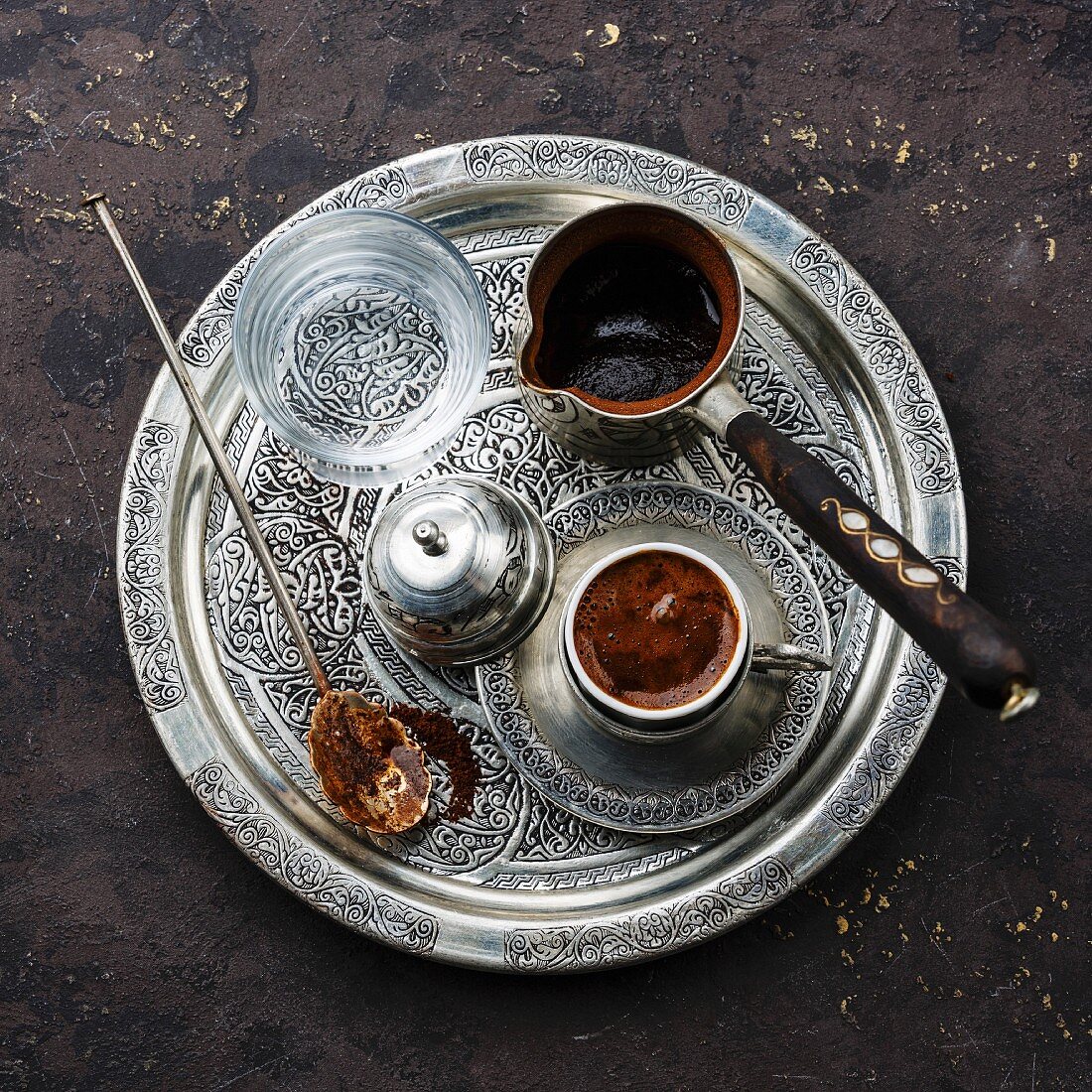 Turkish coffee in coffee pot and cold water on silver tray on black stone background