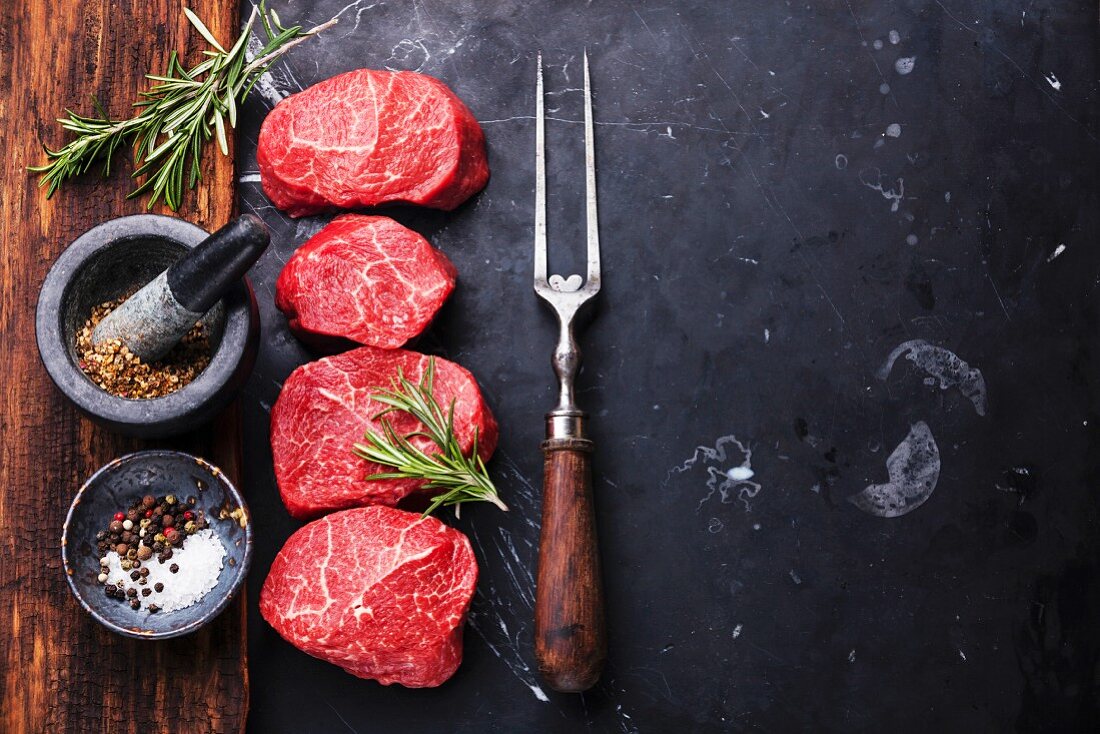 Raw fresh marbled meat Steaks with seasonings and meat fork on dark marble background