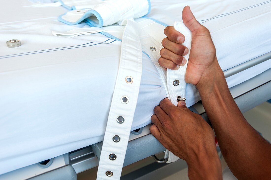 Nurse fastening medical restraint to hospital bed