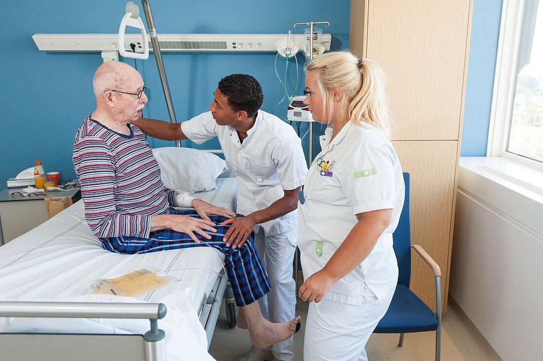 Nurses talking to senior man in hospital bed