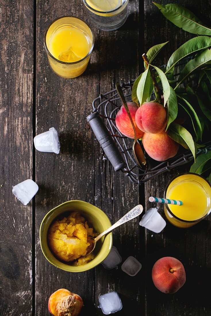 Yellow sorbet, peaches on branch with leaves and glass with peach juice with ice cubes over old wooden table