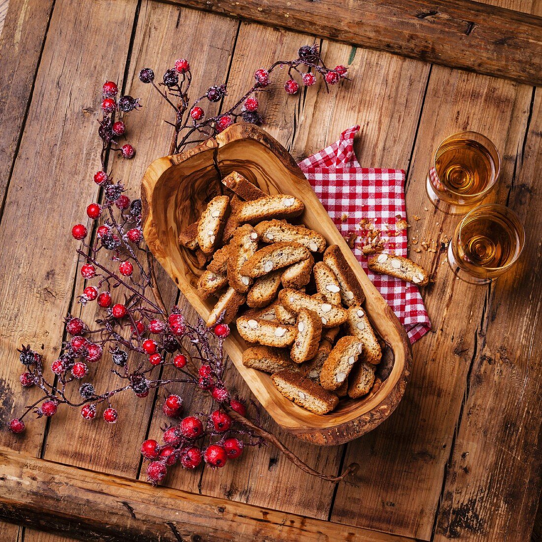 Cantucci in Olivenholz-Schale, Beerenzweig und Dessertwein auf Holzuntergrund