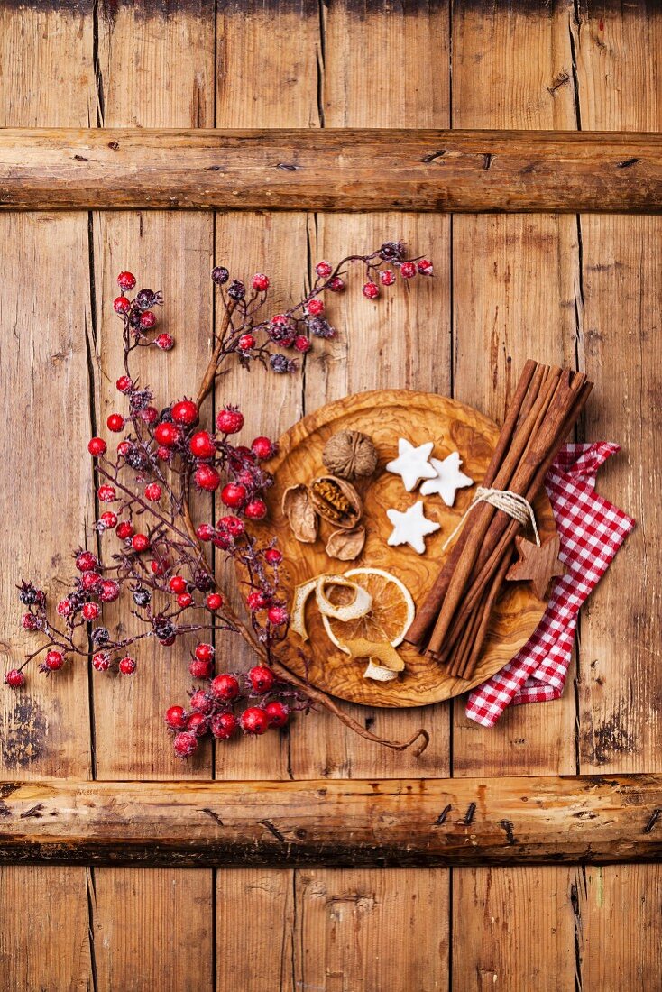 Weihnachtsplätzchen, Walnüsse, getrocknete Orangenschale, Zimtstangen und Beerenzweig auf Holzuntergrund