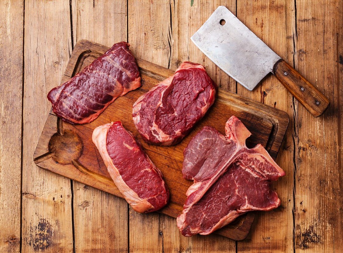 Rohe Steaks und Küchenbeil auf Holzuntergrund
