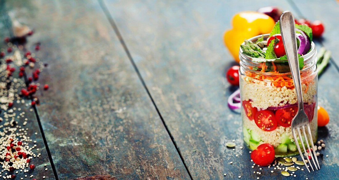 Cucumber, quinoa, tomato, onion, carrot and mint salad in a jar on rustic wooden table