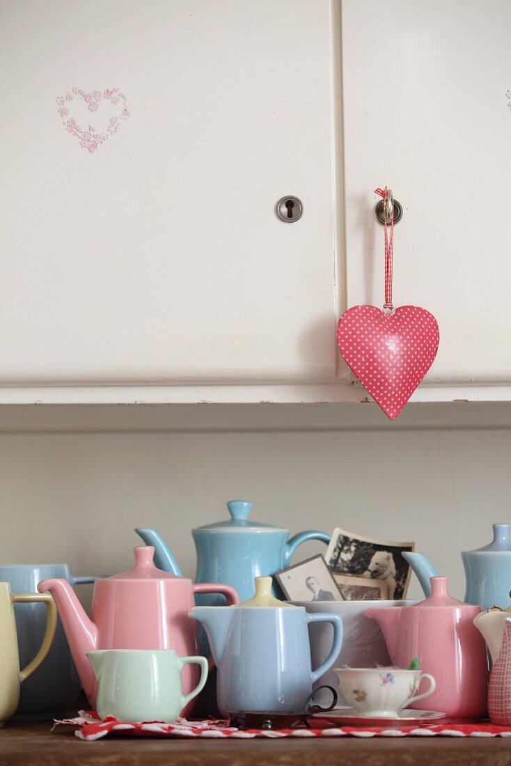 Collection of retro pastel jugs on kitchen dresser with heart-shaped pendant on cupboard door