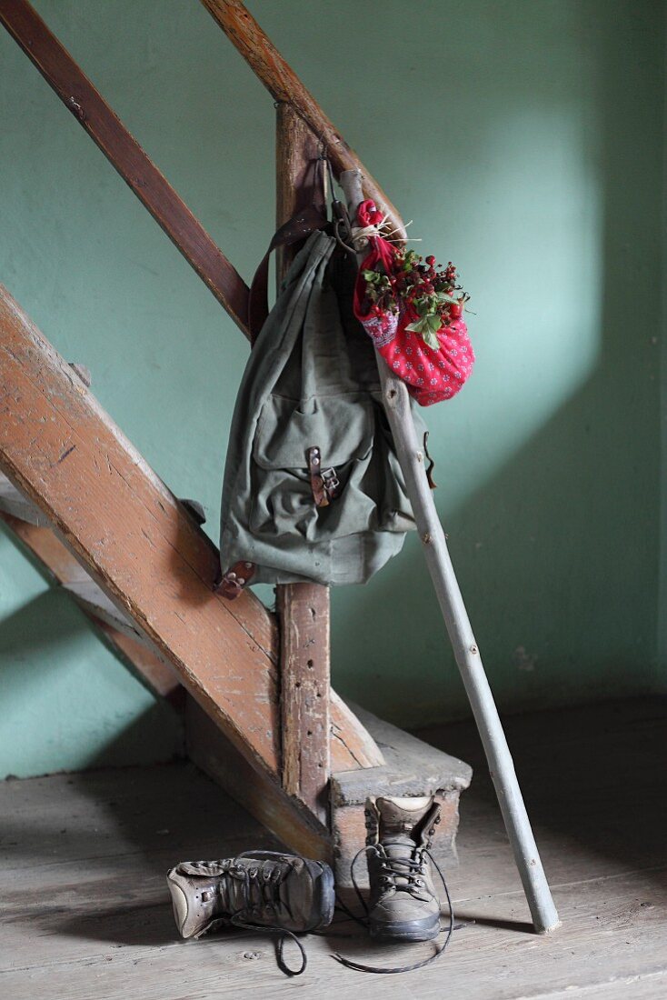 Vintage knapsack, walking stick and bundle of red rose hips on handrail of vintage staircase