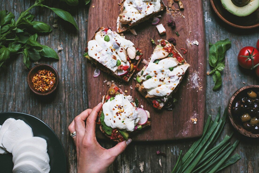 A woman is getting a slice of a chicken caprese sandwich covered with melted mozzarella cheese