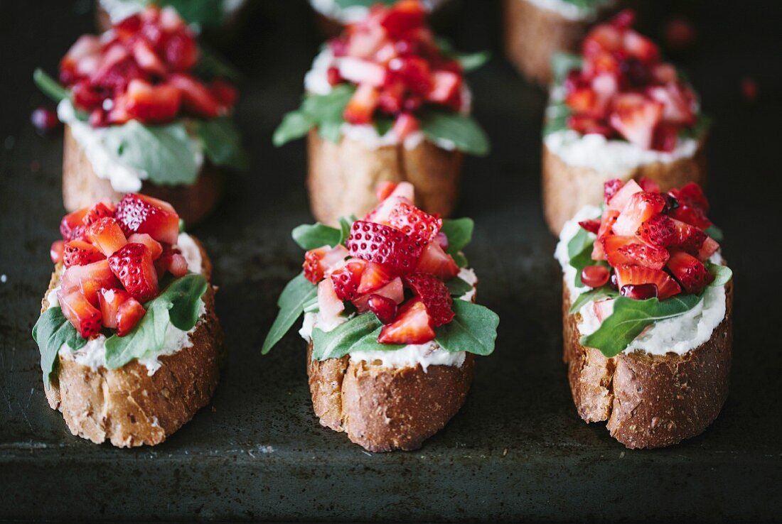 A group of strawberry bruschettas with ricotta cheese and arugula