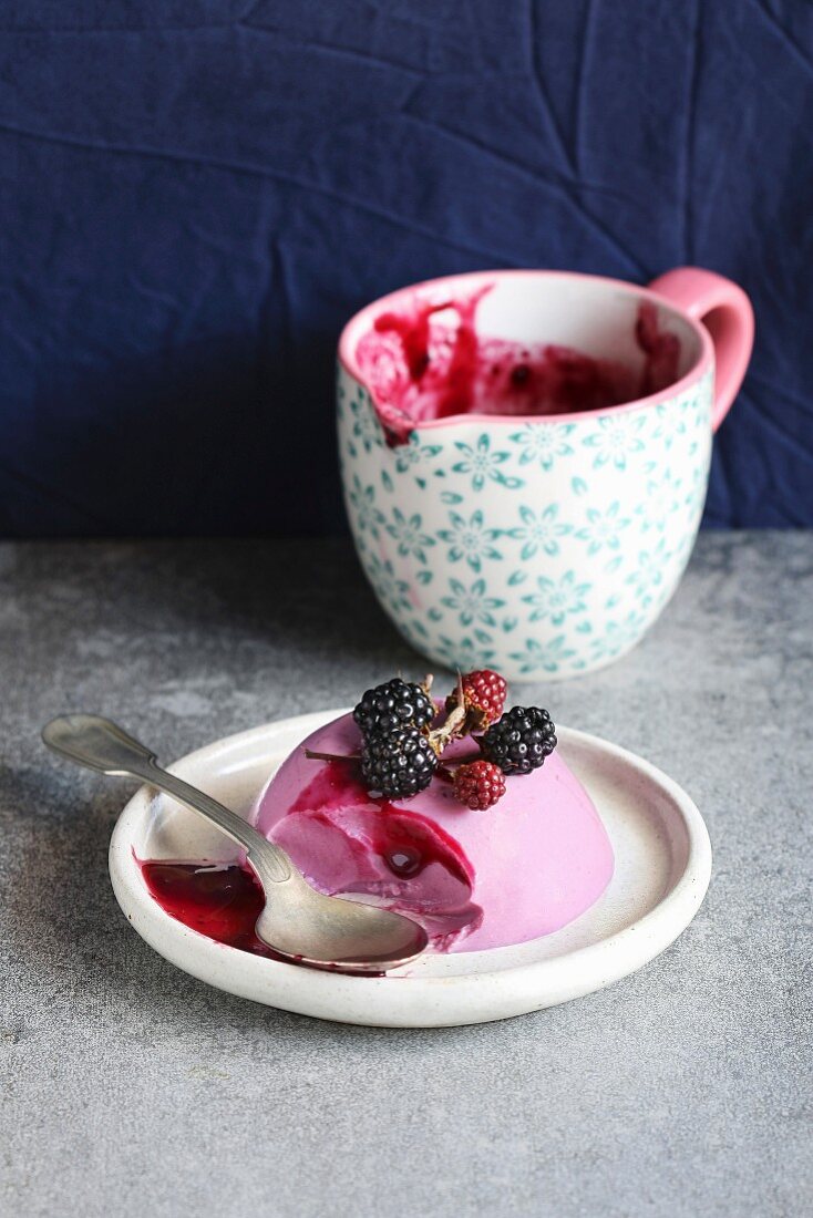 Blackberry panna cotta dessert on a plate decorated with fresh blackberry