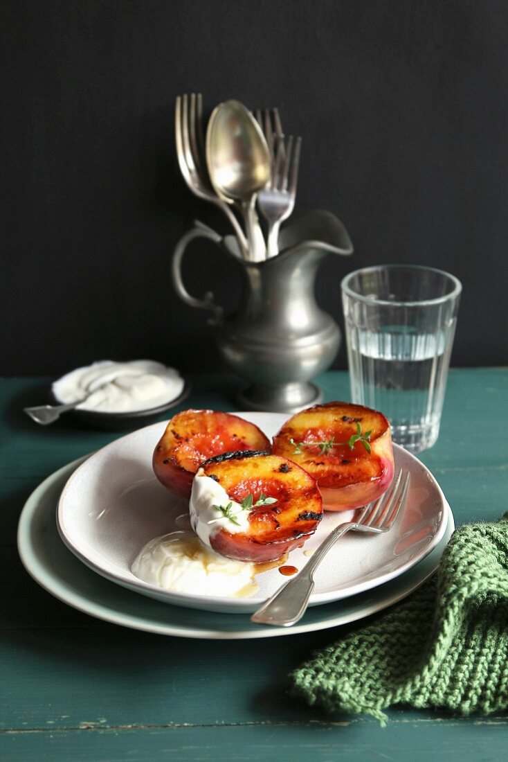 Plate with grilled peach with greek yogurt and honey and decorated with fresh thyme