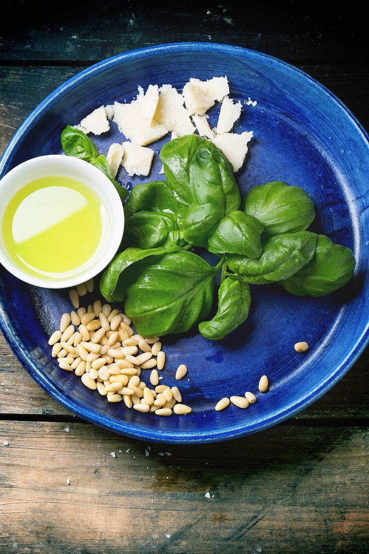 Ingredients for basil pesto served on blue ceramic plate over old wooden table
