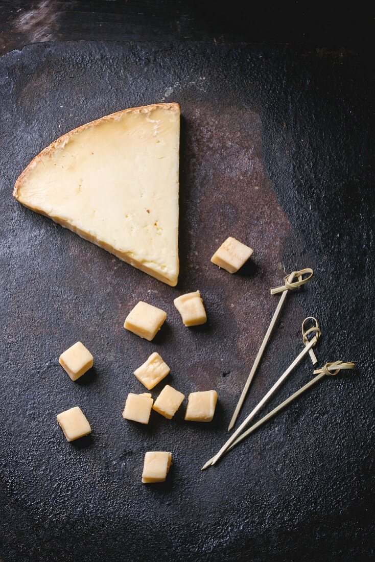 Big piece and little cubes of Belgian cheese over black background