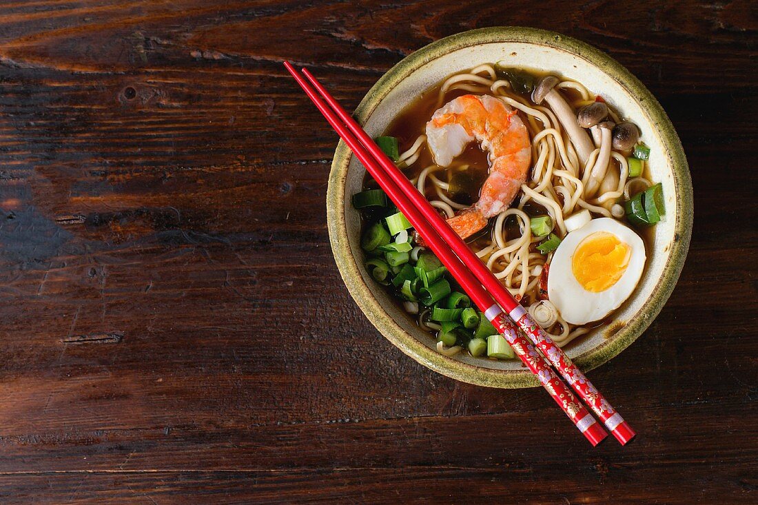 Ceramic bowl of asian ramen soup with shrimp, noodles, spring onion, sliced egg and mushrooms