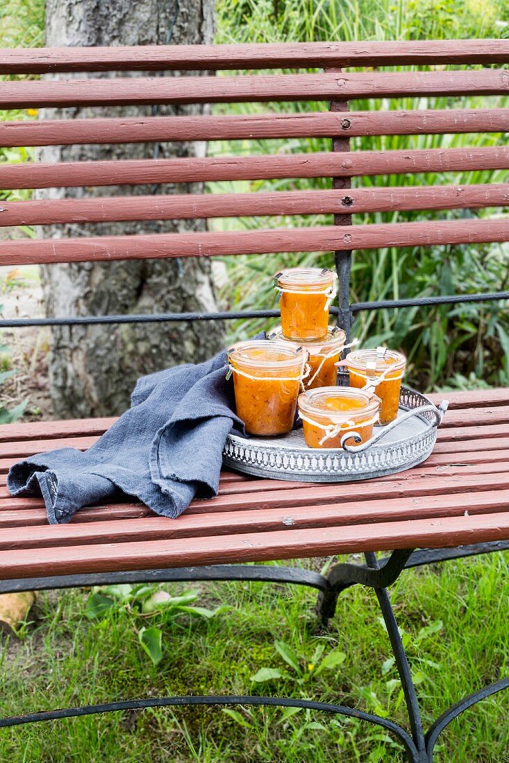 Apricot chutney jars on vintage tray with grey kitchen towel on garden bench