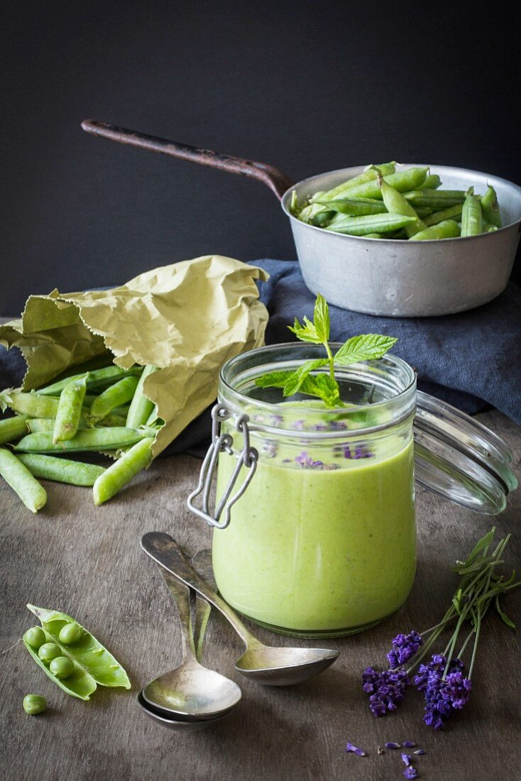 Grüne Gazpacho im Glas daneben Erbsen und Lavendel auf Holztisch