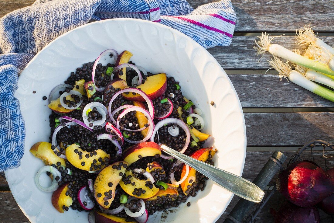 Bowl with lentil and fruit salad on a wooden garden table with kitchen towel