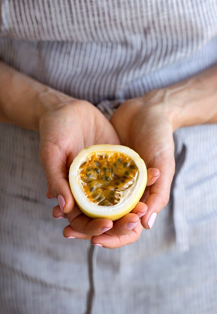 Frau hält die Hälfte einer frisch geschnittenen Passionsfrucht in den Händen