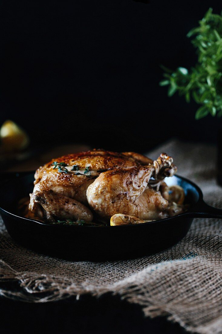 Roasted lemon chicken with a crisp skin displayed in a cast iron skillet right after it came out of the oven