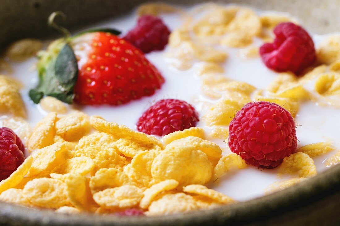 Cornflakes with milk and berries in ceramic bowl