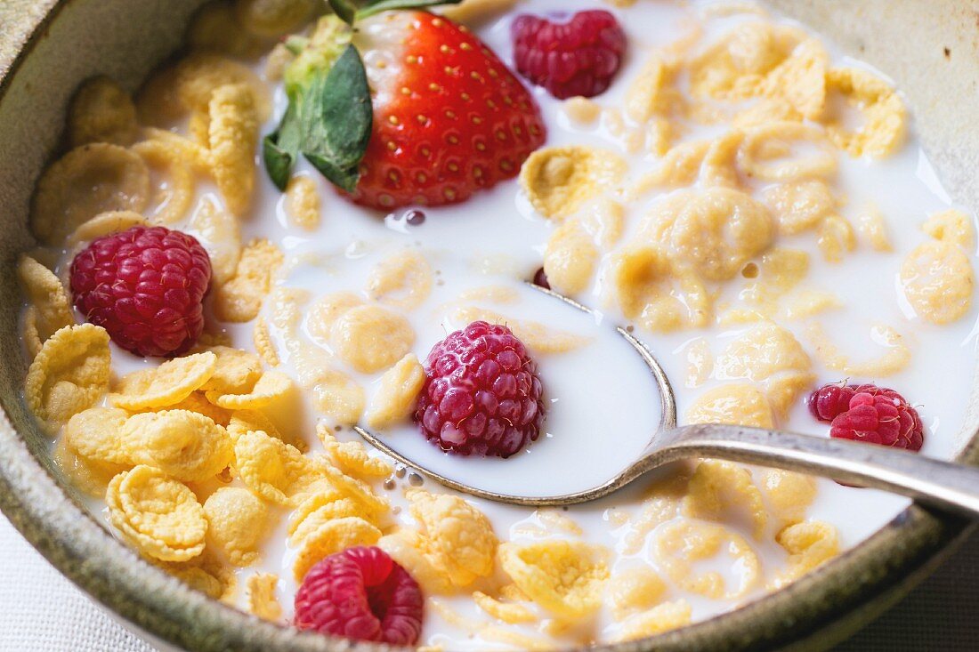 Cornflakes mit Milch und Beeren in Keramikschale (Nahaufnahme)