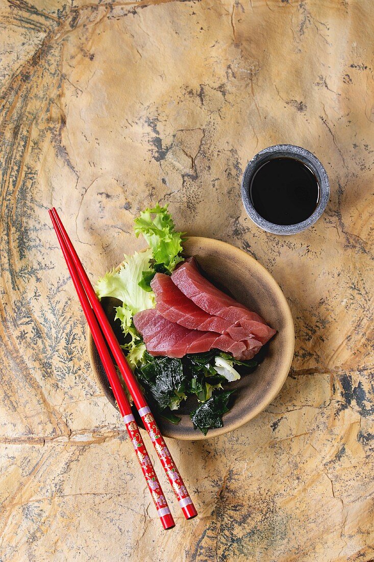 Thunfisch-Sashimi serviert mit Stäbchen und Sojasauce auf Steinoberfläche