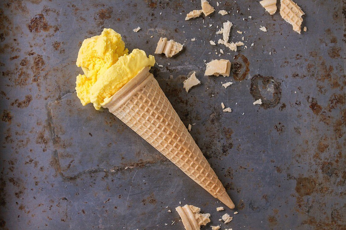 Homemade mango ice cream in waffle cone with wafer crumb over rusty metal textured background