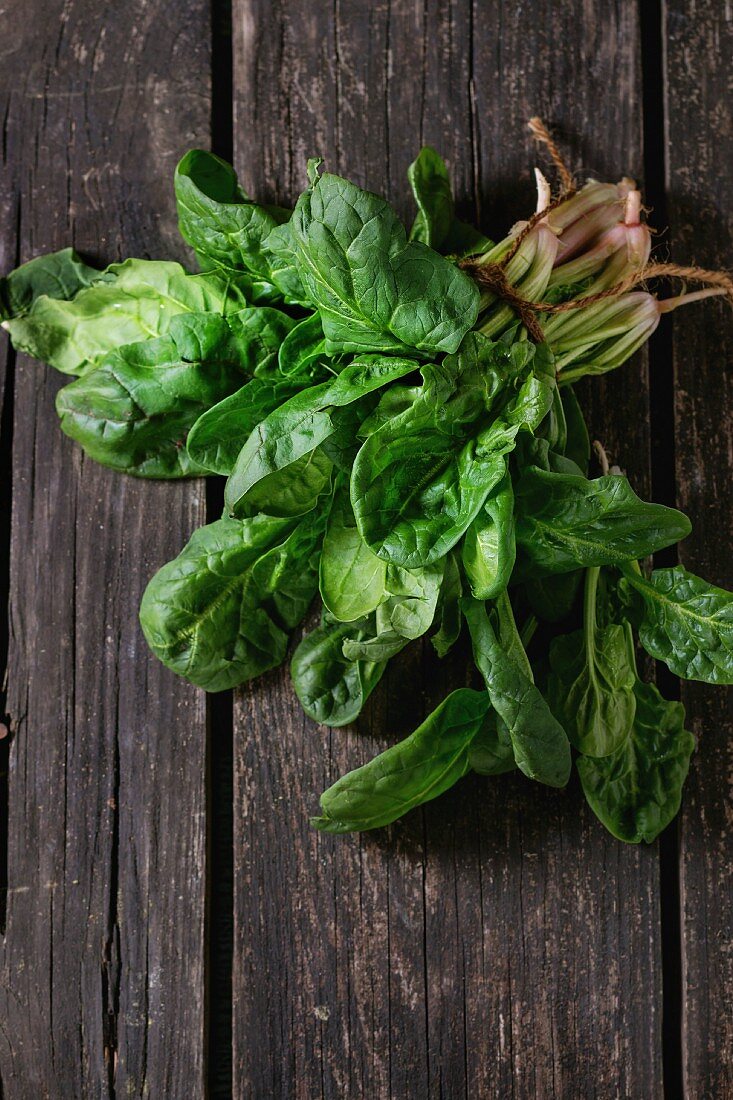 Bunch of fresh spinach with roots over old wooden surface