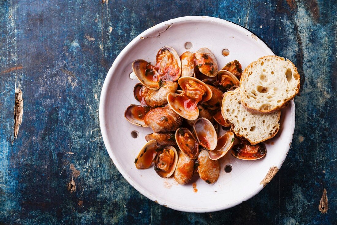 Shells vongole with parsley and tomato sauce in vintage ceramic colander on blue background