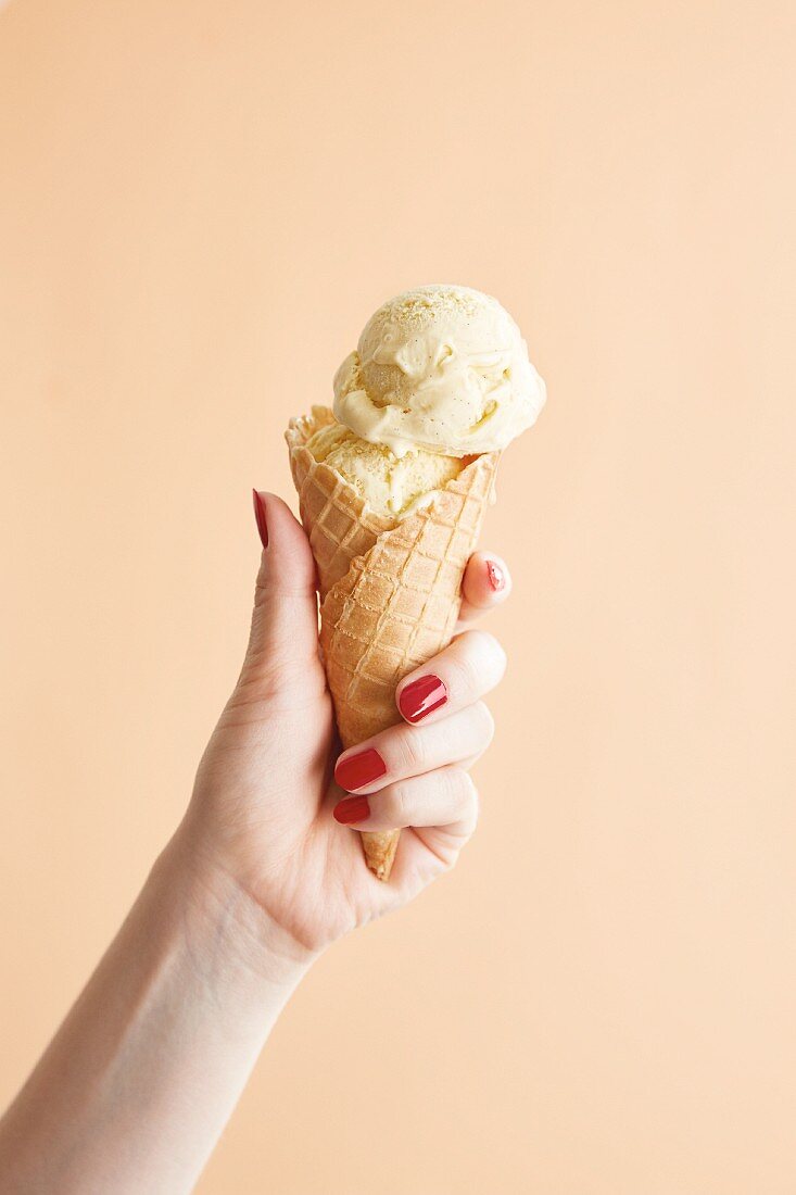 A hand holding a cone filled with vanilla ice cream