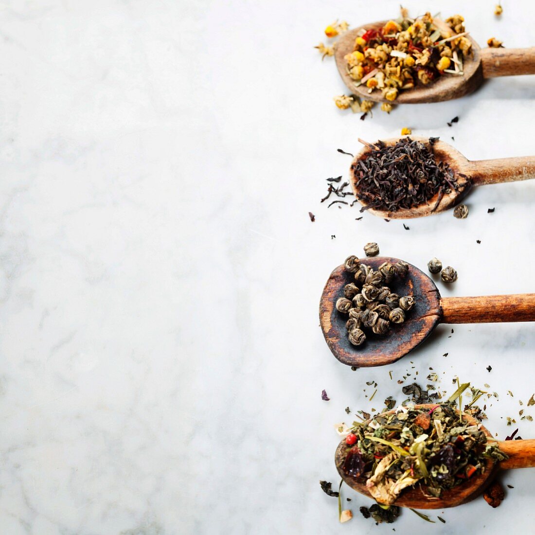 Assortment of dry tea in spoons on marble background