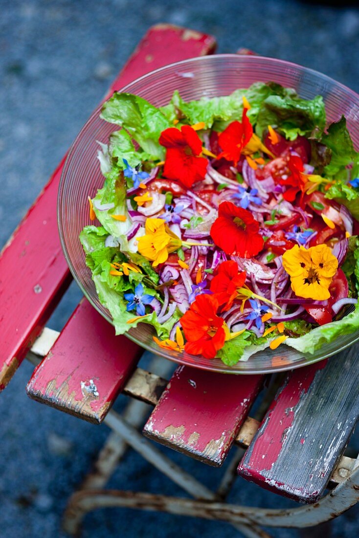 Bunter Salat mit Essblüten in Schüssel auf Gartenstuhl